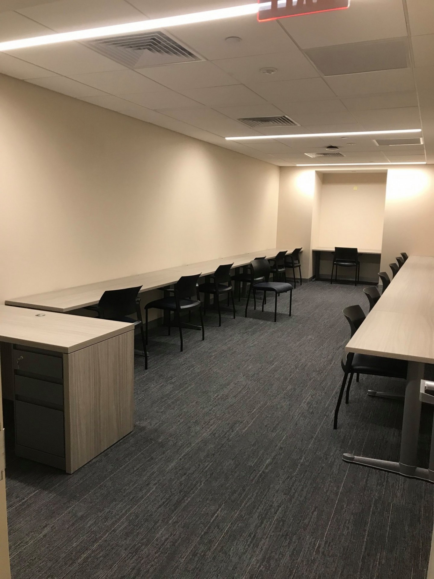 Narrow well-lit room with tables on all sides and chairs against them